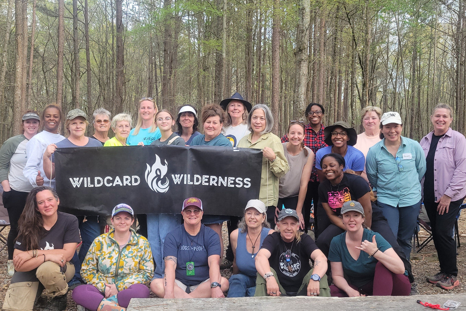 Group of people posing with a Wildcard Wilderness banner in a forest setting.